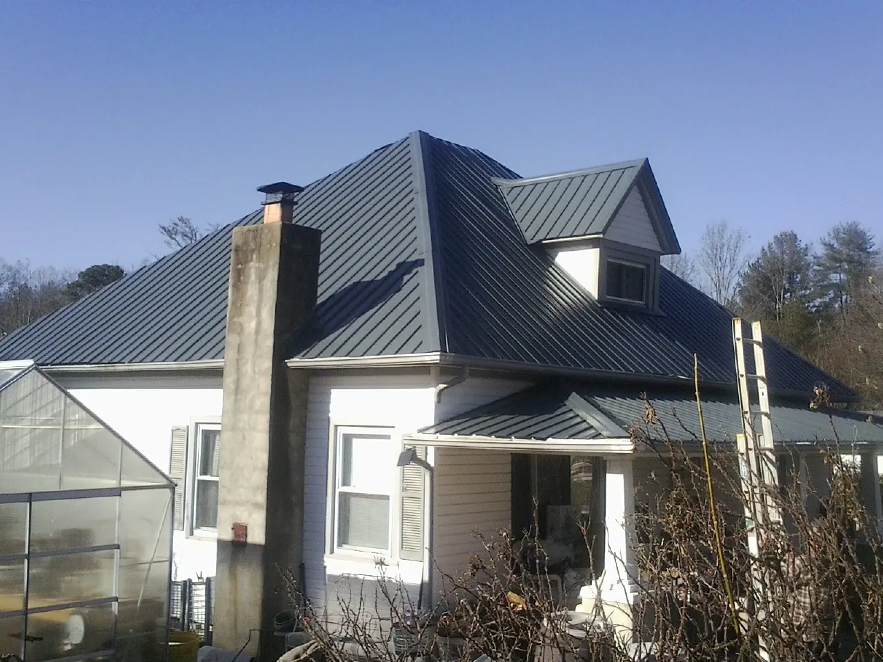 Dark blue standing seam metal roof on a white farmhouse with dormer — Slate & Tile Roof Repair by Roofing Brothers in West Long Branch