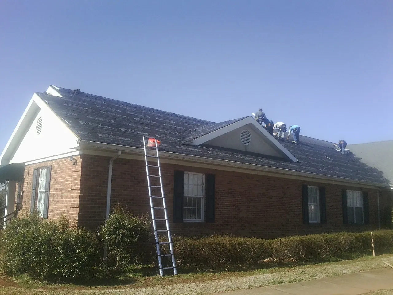Crew tearing shingles off a brick ranch roof with a ladder set — Metal Roof Repair work by our crew in West Long Branch
