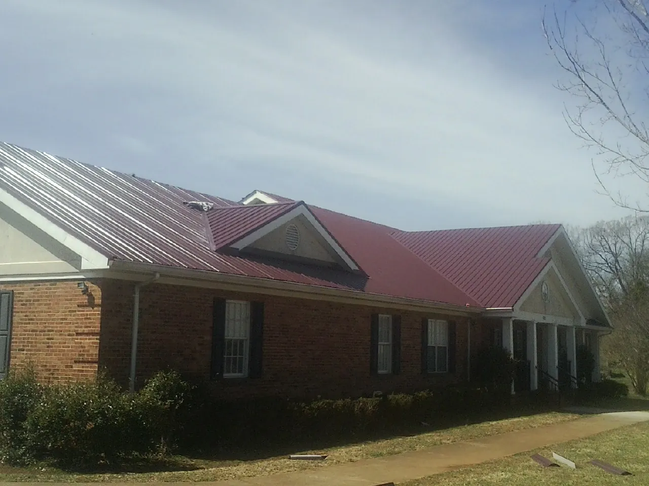 Red metal roof with gabled entries on a long brick building, from a Hail Damage Roof Repair job in West Long Branch