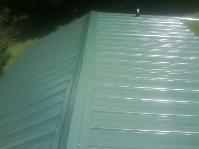 New green metal panels meeting at the ridge of a roof — Flat Roof Repair work by our crew in West Long Branch