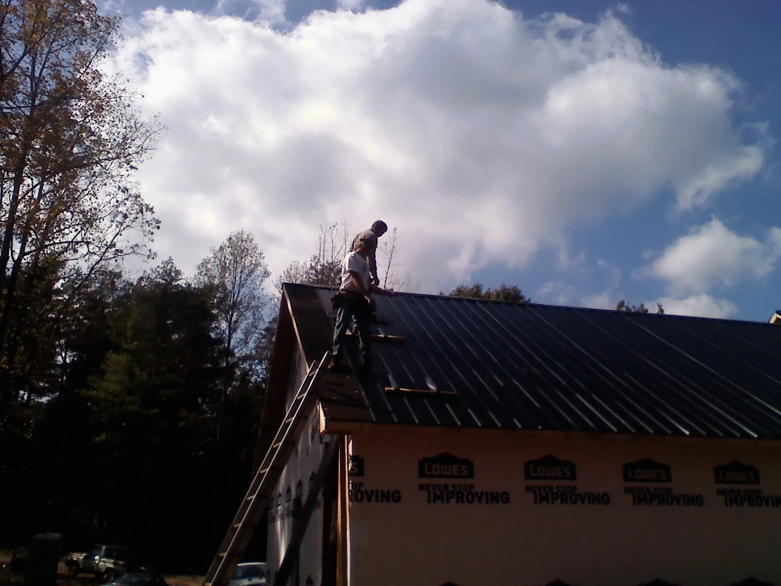 Roofer fastening dark metal panels high against a cloudy sky, from a Roof Inspection job in West Long Branch