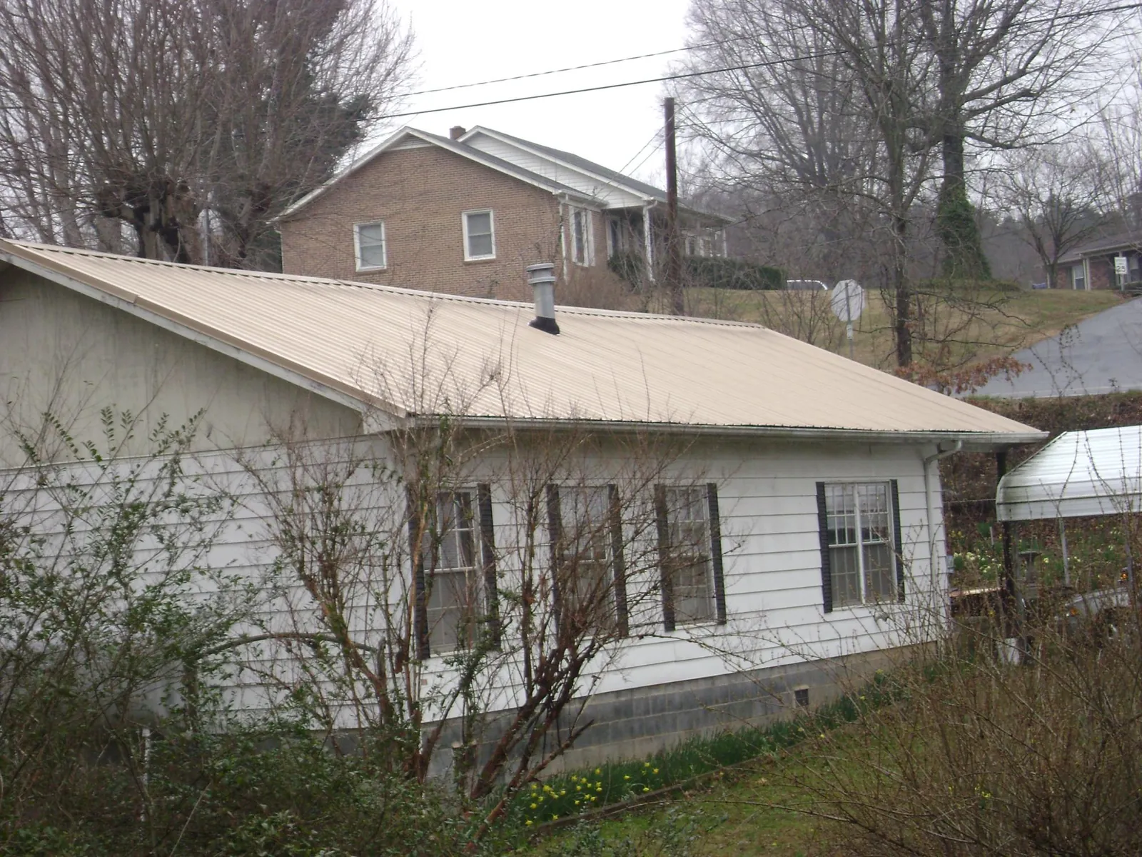 Tan metal roof on a white sided house set into a hillside — Commercial Roofing by Roofing Brothers in West Long Branch